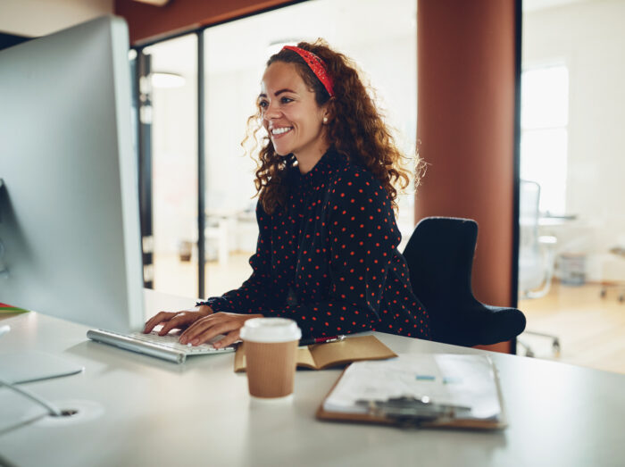 Young businesswoman sitting at her office desk in the afternoon and smiling while working on a computer